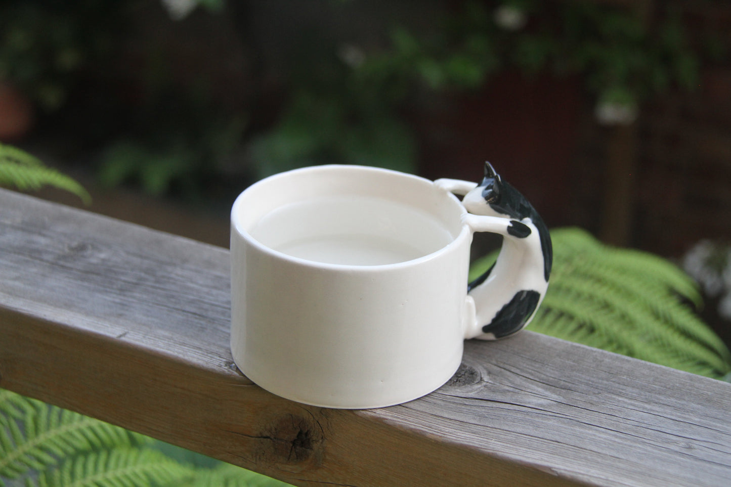 White mug with a black cat design handle on a wooden surface