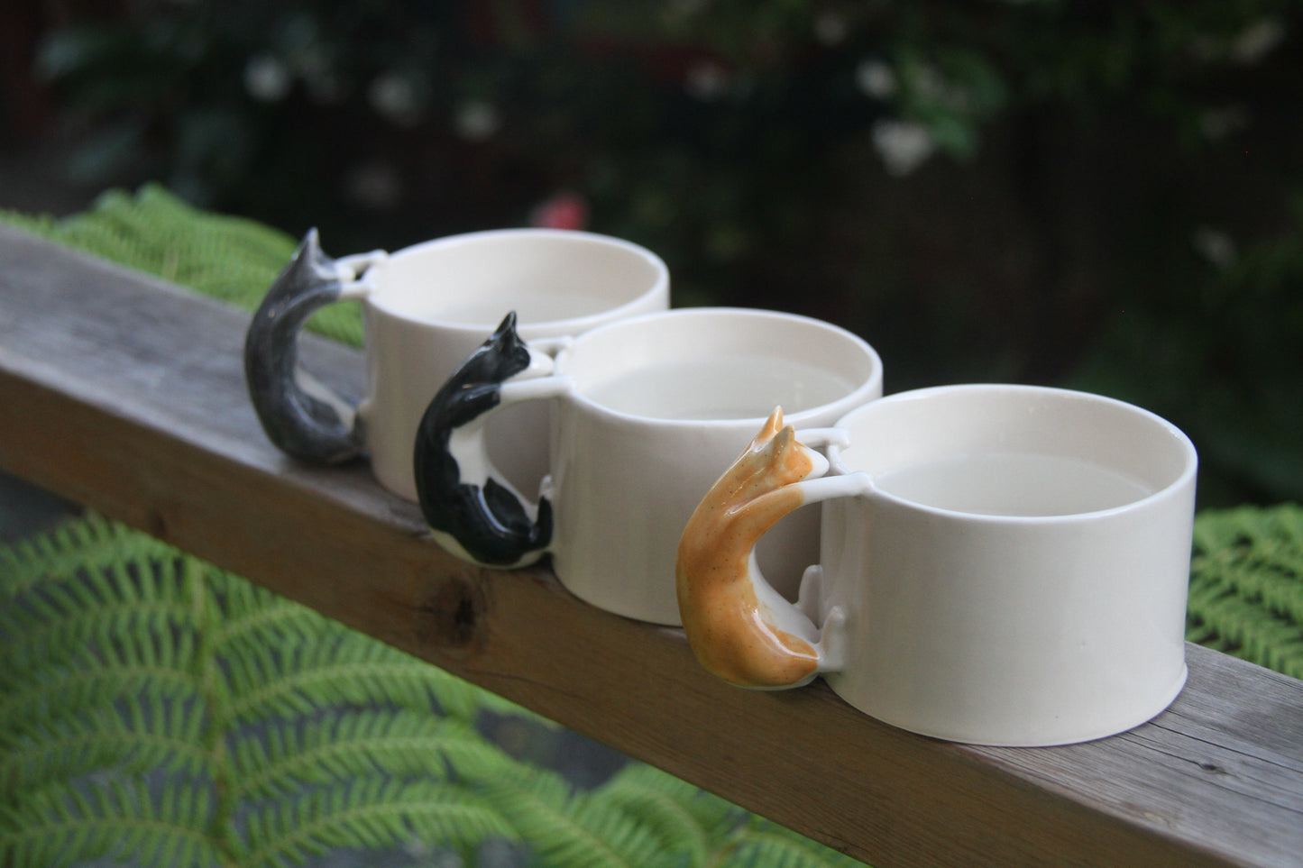 Set of four white mugs with cat-shaped handles on a wooden surface.