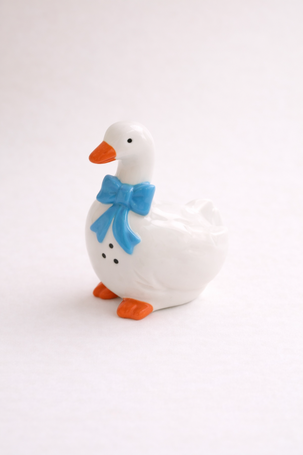 White goose figurine with a blue bow on a white background