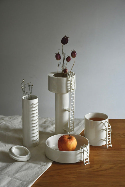 Set of white ceramic vases and bowls on a wooden surface with a gray background
