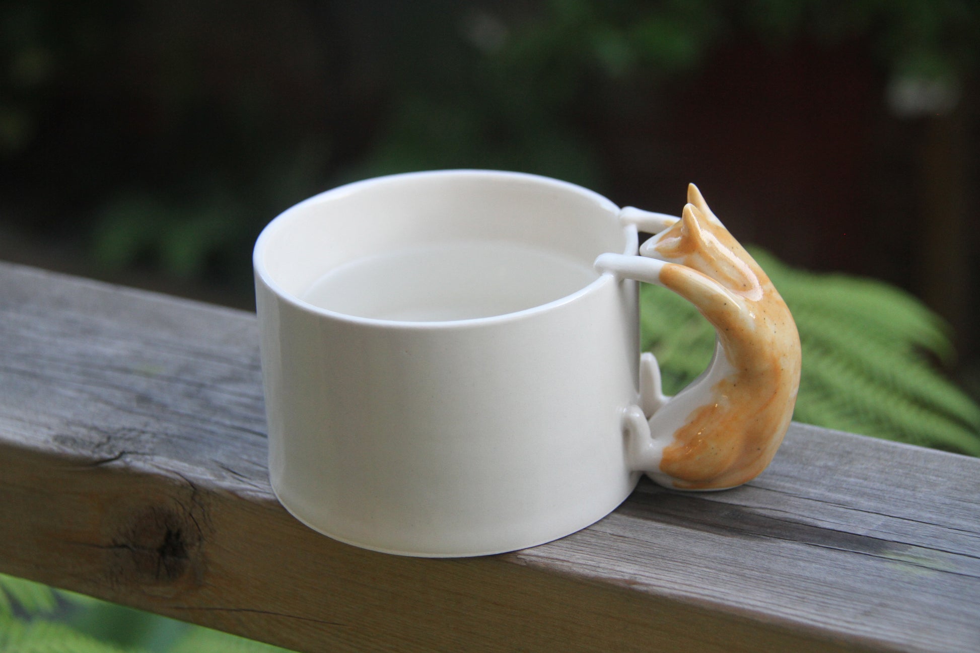 White ceramic mug with a  genger cat handle on a wooden surface