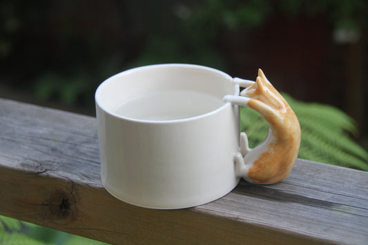 White ceramic mug with a  genger cat handle on a wooden surface