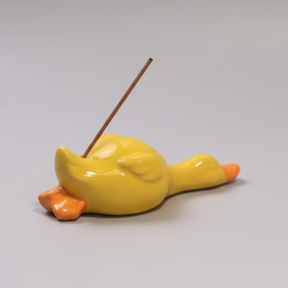 Yellow ceramic duck incense holderon a white surface