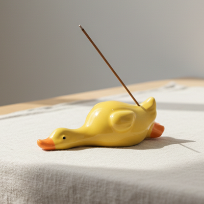 Yellow duck-shaped incense burner with a single incense stick on a light fabric background